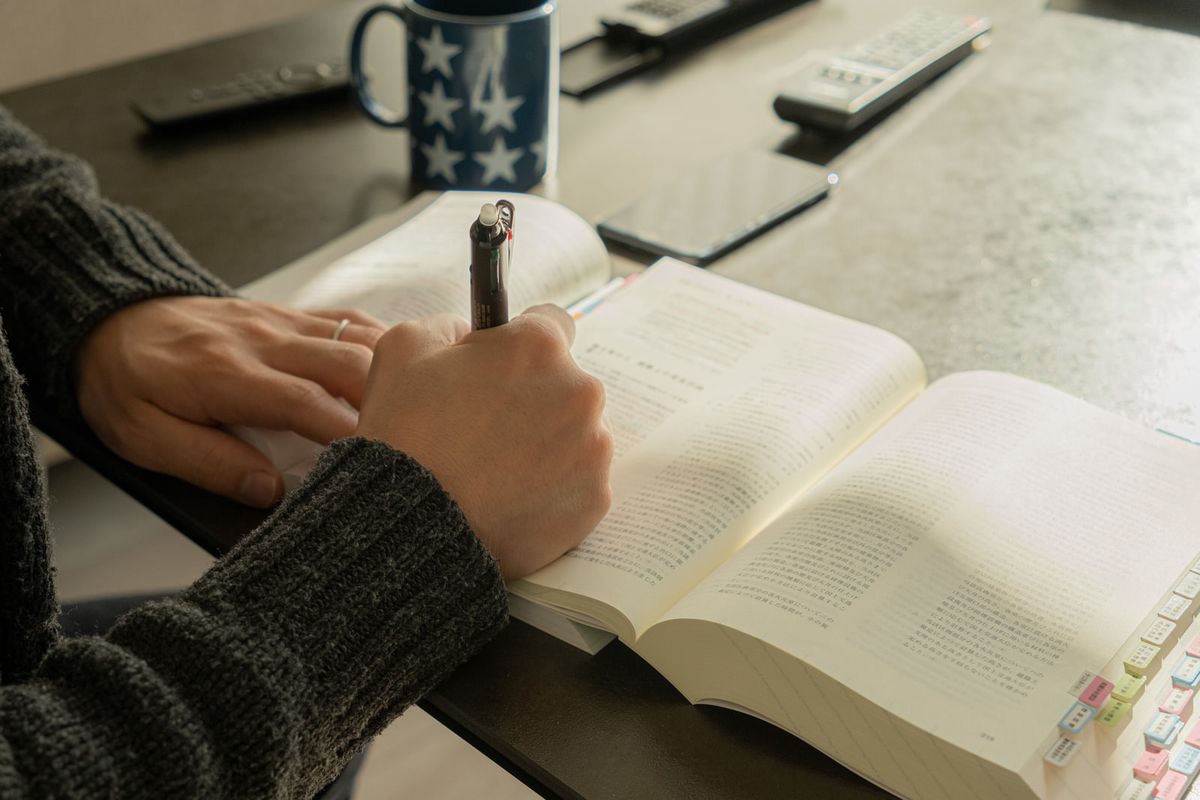 ノートと参考書、ペンを持ち机で学ぶ中高年の手元のクローズアップ