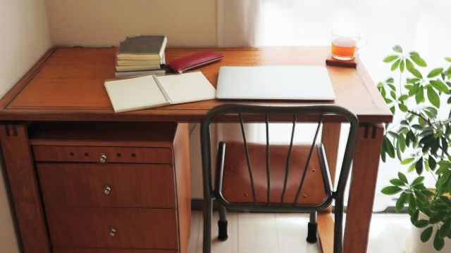 窓際の木製デスクでノートやパソコンを使って学びながら、70代から新しい仕事や複数収入に挑戦するイメージ